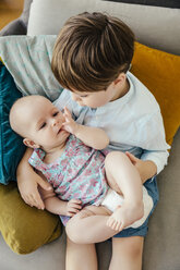 Brother holding his little sister in his arms on couch - MFF001960