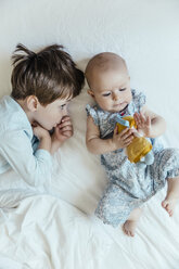 Baby girl and brother lying side by side on bed - MFF001969