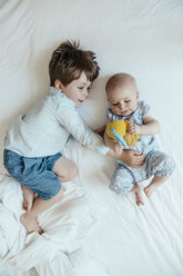 Baby girl and brother lying side by side on bed - MFF001970