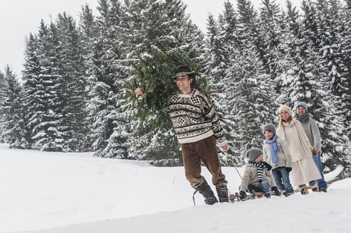 Österreich, Altenmarkt-Zauchensee, Mann mit Weihnachtsbaum und Familie zusammen im Winterwald - HHF005375