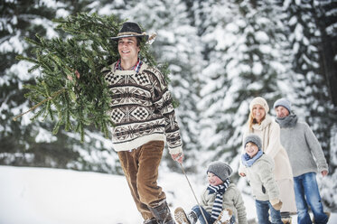 Österreich, Altenmarkt-Zauchensee, Mann mit Weihnachtsbaum und Familie zusammen im Winterwald - HHF005376