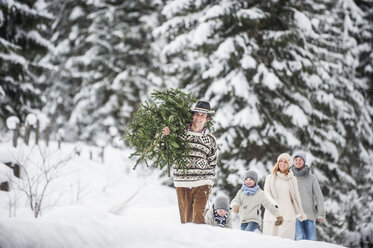Österreich, Altenmarkt-Zauchensee, Mann mit Weihnachtsbaum und Familie zusammen im Winterwald - HHF005377