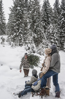 Österreich, Altenmarkt-Zauchensee, Mann mit Weihnachtsbaum und Familie zusammen im Winterwald - HHF005384