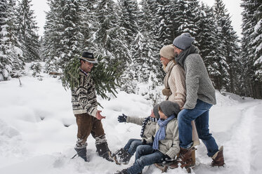 Österreich, Altenmarkt-Zauchensee, Mann mit Weihnachtsbaum und Familie zusammen im Winterwald - HHF005385