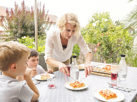 Mutter und ihre beiden Söhne essen zusammen Pizza auf der Terrasse - LAF001459