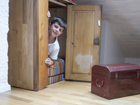 Porträt eines kleinen Jungen, der in einem Schrank in seinem Zimmer sitzt, lizenzfreies Stockfoto