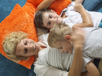 Mother and her two sons relaxing together on carpet at home - LAF001466