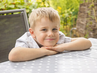 Porträt eines lächelnden blonden Jungen, der auf der Terrasse sitzt - LAF001470