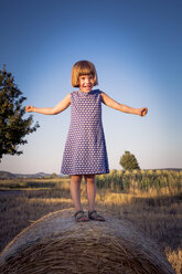 Porträt eines kleinen Mädchens, das mit ausgestreckten Armen auf einem Strohballen steht - LVF003763