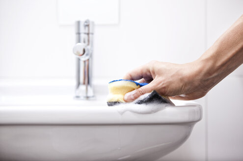 Woman cleaning bathroom sink with sponge - MFRF000340