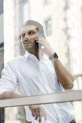 Geschäftsmann lehnt sich gegen eine Fensterscheibe und telefoniert mit seinem Smartphone - PESF000034