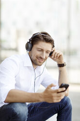 Porträt eines lächelnden Mannes, der mit MP3-Player und Kopfhörern Musik hört - PESF000005