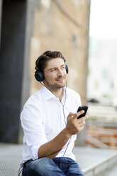 Porträt eines lächelnden Mannes, der mit MP3-Player und Kopfhörern Musik hört - PESF000006