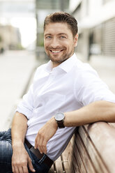 Porträt eines lächelnden Mannes mit weißem Hemd, der auf einer Holzbank sitzt - PESF000021