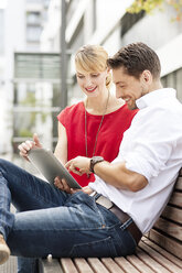 Couple sitting side by side on wooden bench using digital tablet - PESF000023