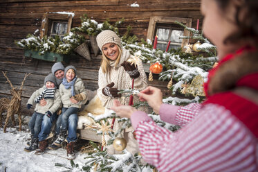 Österreich, Altenmarkt-Zauchensee, Familie beim Schmücken des Weihnachtsbaums vor einem Bauernhaus - HHF005403