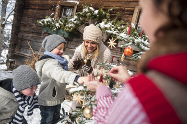 Österreich, Altenmarkt-Zauchensee, Familie beim Schmücken des Weihnachtsbaums vor einem Bauernhaus - HHF005395