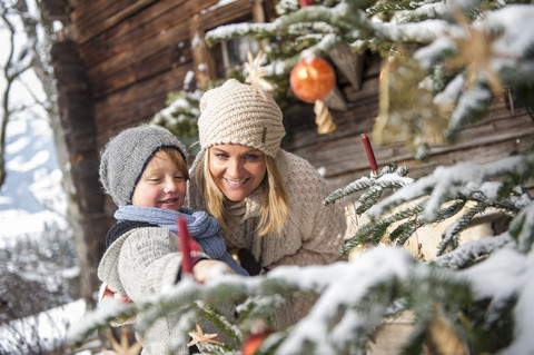 Österreich, Altenmarkt-Zauchensee, Mutter und Sohn betrachten den geschmückten Weihnachtsbaum vor einem Bauernhaus, lizenzfreies Stockfoto