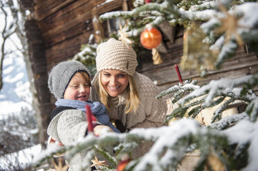 Österreich, Altenmarkt-Zauchensee, Mutter und Sohn betrachten den geschmückten Weihnachtsbaum vor einem Bauernhaus - HHF005396