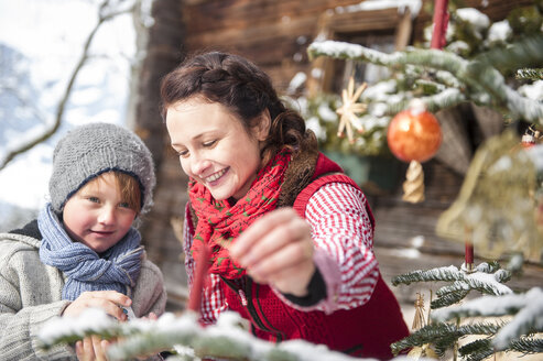 Österreich, Altenmarkt-Zauchensee, Frau und Junge beim Schmücken des Weihnachtsbaums vor einem Bauernhaus - HHF005397