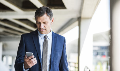 Älterer Geschäftsmann auf Parkdeck mit Mobiltelefon - UUF005284