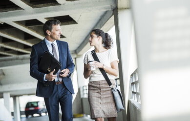 Mature businessman and young colleague walking in parking garage, talking - UUF005298