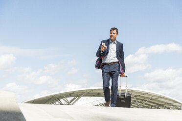 Businessman on business trip arriving with trolley - UUF005303