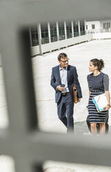 Mature businessman and young woman with trolley walking in yard - UUF005312