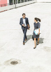 Mature businessman and young woman with trolley walking in yard - UUF005313