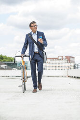 Businessman pushing bike while talking on the phone - UUF005331
