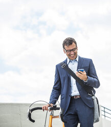 Businessman with bike using smartphone - UUF005335