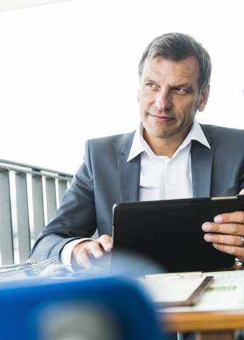 Geschäftsmann, der im Freien sitzt und ein digitales Tablet benutzt, lizenzfreies Stockfoto