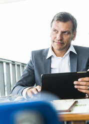 Geschäftsmann, der im Freien sitzt und ein digitales Tablet benutzt - UUF005212