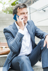 Geschäftsmann sitzt auf einer Treppe und benutzt ein Smartphone - UUF005223