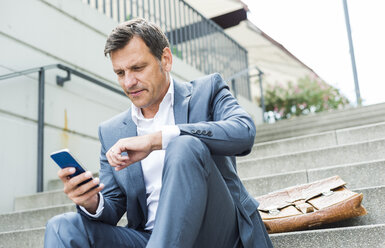 Businessman sitting on stairs using smart phone - UUF005224