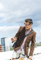 Mature man with bicycle using smart phone - UUF005263