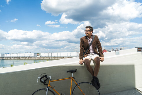 Älterer Mann mit Fahrrad sitzt an der Wand und genießt das Wetter - UUF005264