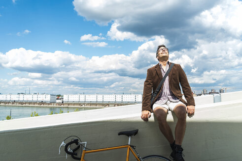 Älterer Mann mit Fahrrad sitzt an der Wand und genießt das Wetter - UUF005265