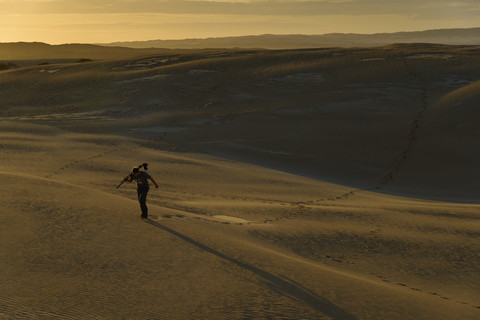 Südaustralien, Mann mit Stativ und Kamera beim Spaziergang durch Sanddünen in der Dämmerung, lizenzfreies Stockfoto