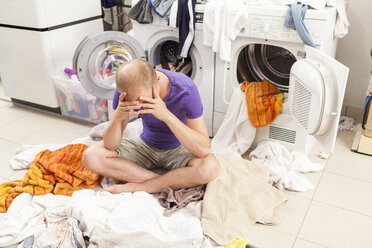 Young man sitting between dirty laundry - JUNF000412