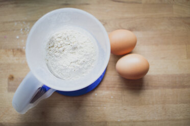Measuring cup of flour and two brown eggs on wood - ASCF000311