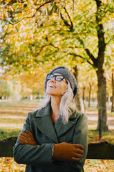 Smiling woman with crosssed arms wearing wooly hat and gloves looking up - CHAF001121