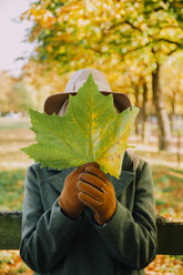 Frau versteckt ihr Gesicht hinter einem Herbstblatt - CHAF001123