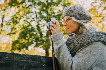 Frau beim Fotografieren mit einer alten Kamera in einem herbstlichen Park - CHAF001131