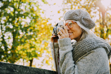 Frau beim Fotografieren mit einer alten Kamera in einem herbstlichen Park - CHAF001132