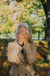 Woman in autumnal park hiding her face behind hands - CHAF001143