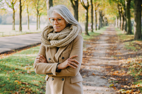 Porträt einer Frau mit Schal und Brille, die in einem herbstlichen Park spazieren geht, lizenzfreies Stockfoto