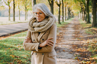 Porträt einer Frau mit Schal und Brille, die in einem herbstlichen Park spazieren geht - CHAF001147