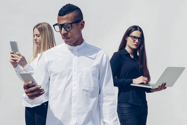 Drei stilvolle junge Menschen mit Mini-Tablet, Smartphone und Laptop vor weißem Hintergrund - CHAF001166