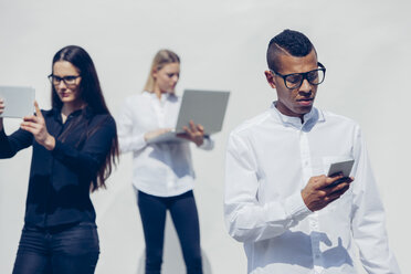Drei stilvolle junge Menschen mit Mini-Tablet, Smartphone und Laptop vor weißem Hintergrund - CHAF001170